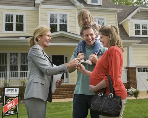 A Kaplan trained real estate agent handing the keys to a young family in front of their new house