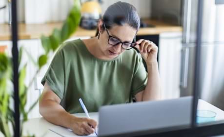 Woman sitting in front of a laptop taking notes while studying with her online Kaplan training course