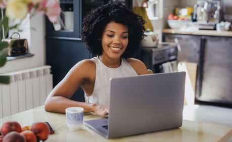 Woman sitting in front of a laptop taking notes while studying with her online Kaplan training course